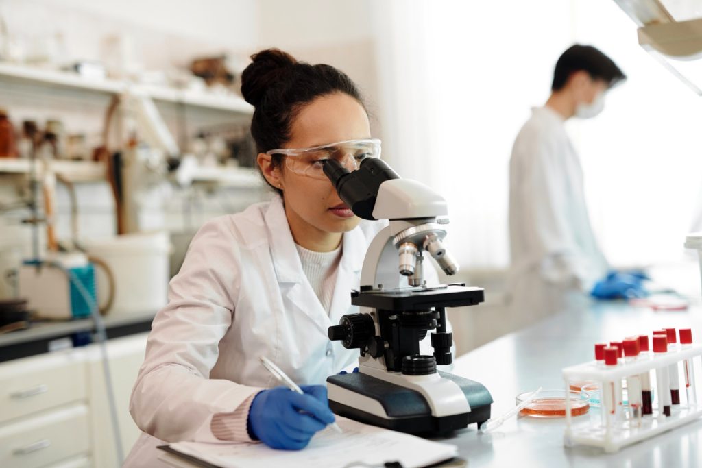 Mujer investigadora en un laboratorio observando muestras a través de un microscopio